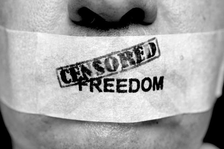 A persons lips taped up, with the words censored freedom written on the tape